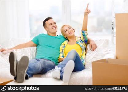 moving, home and couple concept - smiling couple relaxing on sofa and pointing finger in new home