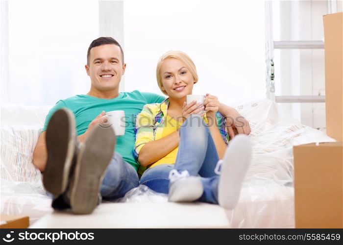 moving, home and couple concept - smiling couple relaxing on sofa with tea cups in new home