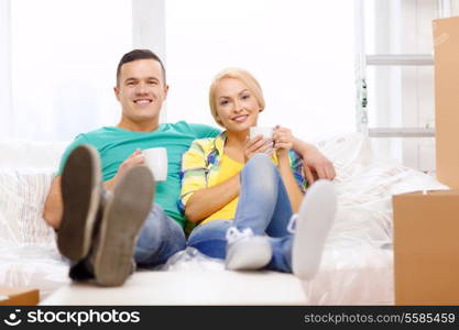 moving, home and couple concept - smiling couple relaxing on sofa with tea cups in new home