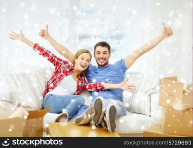 moving, home and couple concept - smiling couple showing thumbs up and waving hands on sofa in new home