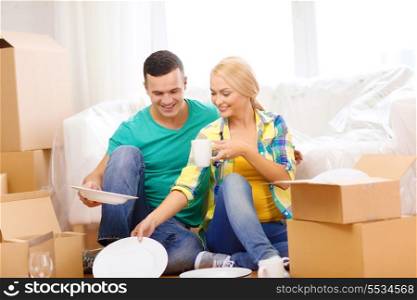 moving, home and couple concept - smiling couple unpaking boxes with kitchenware in new home