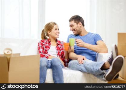 moving, home and couple concept - smiling couple with coffee or tea cups relaxing on sofa in new home