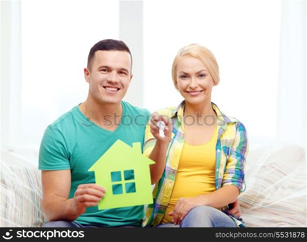 moving, home and couple concept - smiling couple with green house and keys in new home