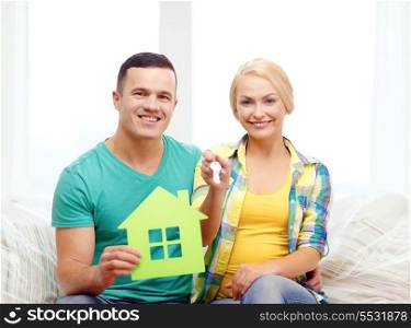 moving, home and couple concept - smiling couple with green house and keys in new home