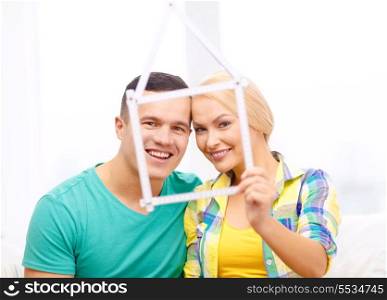 moving, home and couple concept - smiling couple with house from measuring tape at new home