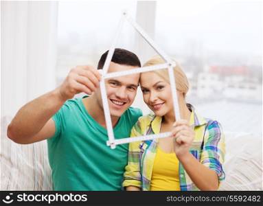 moving, home and couple concept - smiling couple with house from measuring tape at new home