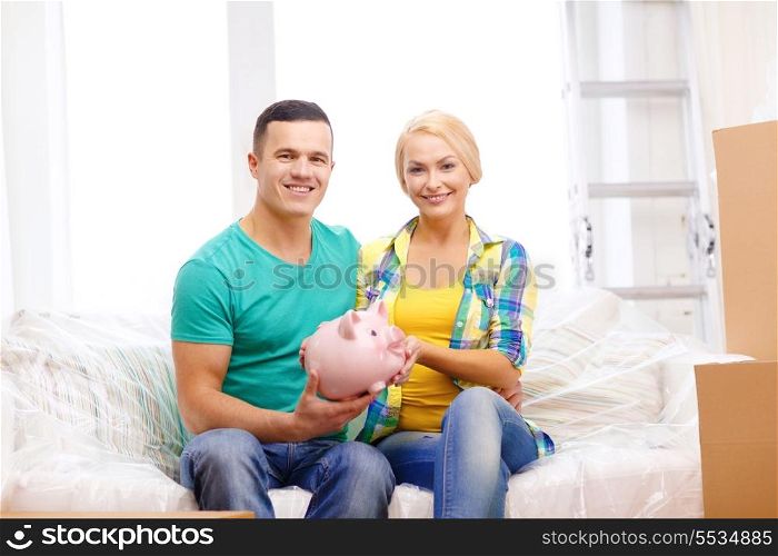 moving, home and couple concept - smiling couple with piggybank in new home