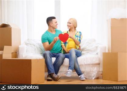moving, home and couple concept - smiling couple with red heart on sofa in new home