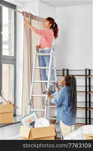 moving, home improvement and real estate concept - happy smiling women with ladder hanging curtain. woman on ladder hanging curtains at home