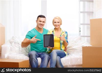 moving, home, technology and couple concept - smiling couple relaxing on sofa and pointing finger to tablet pc computer in new home
