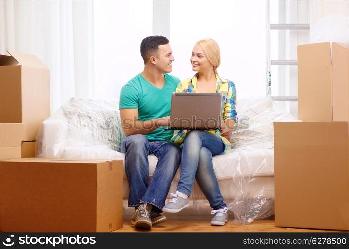 moving, home, technology and couple concept - smiling couple relaxing on sofa with laptop in new home