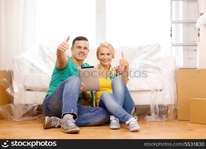 moving, home, technology and couple concept - smiling couple sitting on the floor with tablet pc computer showing thumbs up in new home