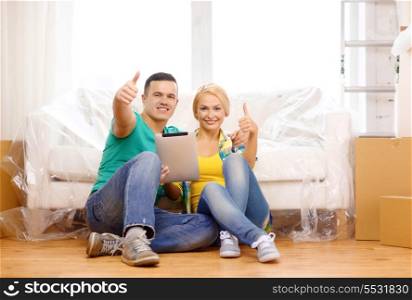 moving, home, technology and couple concept - smiling couple sitting on the floor with tablet pc computer showing thumbs up in new home