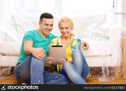 moving, home, technology and couple concept - smiling couple sitting on the floor with tablet pc computer in new home