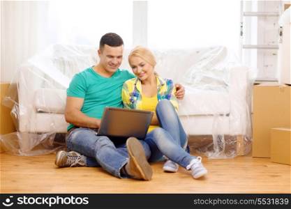 moving, home, technology and couple concept - smiling couple with laptop sitting on floor in new house