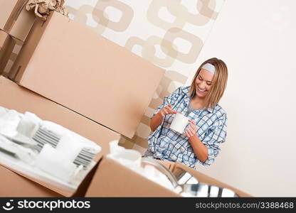 Moving house: Happy woman with box holding cup of coffee in new home