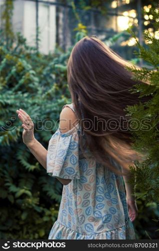 Moving long hair scenic photography. Summertime day. Picture of woman with garden and house on background. High quality wallpaper. Photo concept for ads, travel blog, magazine, article. Moving long hair scenic photography