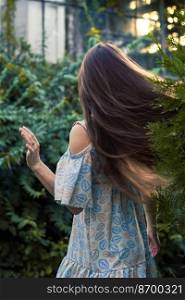 Moving long hair scenic photography. Summertime day. Picture of woman with garden and house on background. High quality wallpaper. Photo concept for ads, travel blog, magazine, article. Moving long hair scenic photography