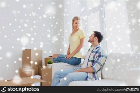 moving, people and real estate concept - happy couple with cardboard boxes on sofa at new home over snow