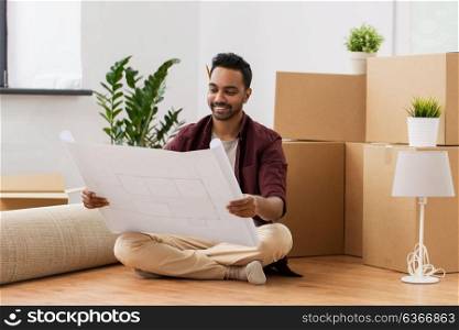 moving, people and real estate concept - happy indian man blueprint and boxes at new home. man with blueprint and boxes moving to new home