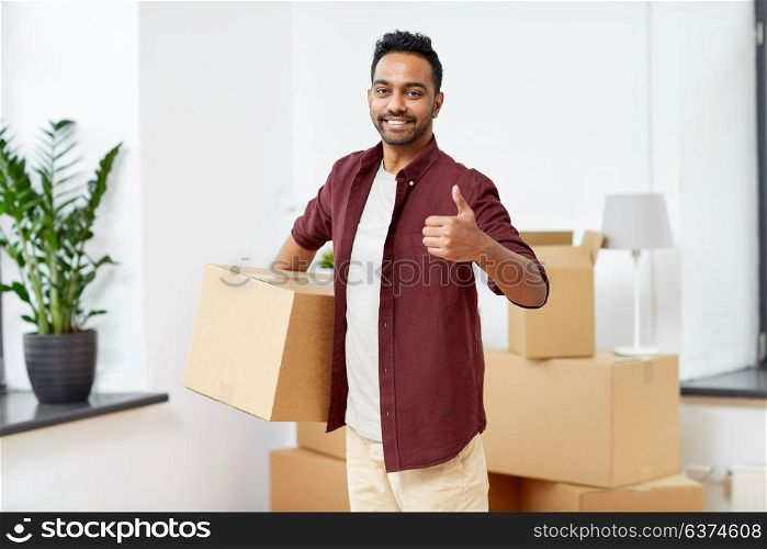 moving, people and real estate concept - happy indian man with boxes at new home showing thumbs up. man with box moving to new home showing thumbs up