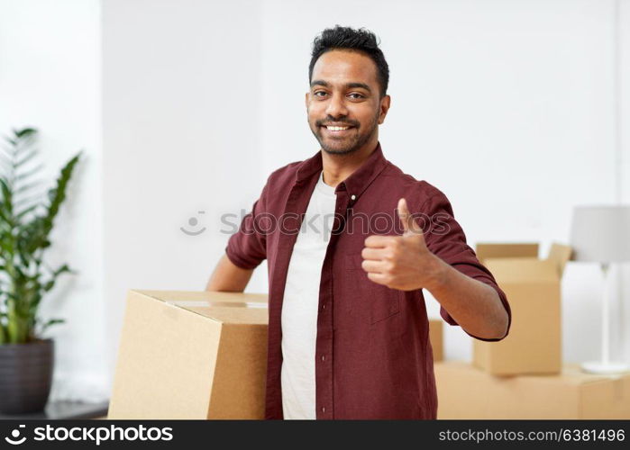 moving, people and real estate concept - happy indian man with boxes at new home showing thumbs up. man with box moving to new home showing thumbs up