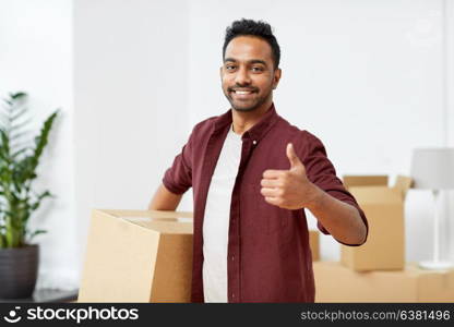 moving, people and real estate concept - happy indian man with boxes at new home showing thumbs up. man with box moving to new home showing thumbs up