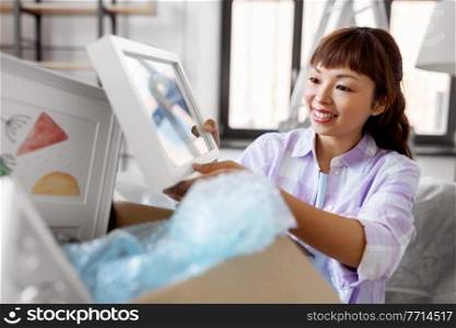 moving, people and real estate concept - happy smiling asian woman unpacking boxes at new home. happy woman unpacking boxes and moving to new home