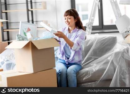 moving, people and real estate concept - happy smiling asian woman unpacking boxes at new home. happy woman unpacking boxes and moving to new home