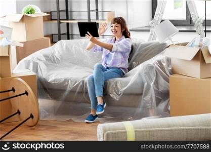 moving, people and real estate concept - happy smiling asian woman with tablet pc computer and boxes having video call at new home. woman with tablet pc having video call at new home