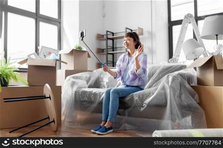moving, people and real estate concept - happy smiling asian woman with smartphone and selfie stick having video call at new home. woman having video call and moving into new home