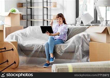 moving, people and real estate concept - happy smiling asian woman with tablet pc computer and boxes having video call at new home. woman with tablet pc having video call at new home