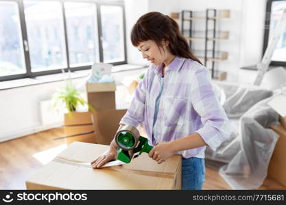 moving, people and real estate concept - happy smiling asian woman with adhesive tape packing box at new home. woman with adhesive tape packing box at new home