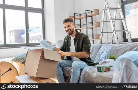 moving, people and real estate concept - happy smiling man unpacking boxes at new home. happy man unpacking boxes and moving to new home