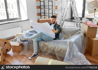 moving, people and real estate concept - happy smiling man with blueprint and boxes at new home. happy man with blueprint moving to new home