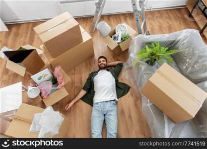 moving, people and real estate concept - happy smiling man with boxes lying on floor at new home. happy man with boxes moving to new home