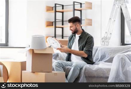 moving, people and real estate concept - happy smiling man with boxes and clock at new home. happy man unpacking boxes and moving to new home