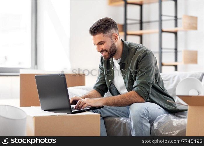 moving, people and real estate concept - happy smiling man with laptop computer at new home. man with laptop computer and moving into new home