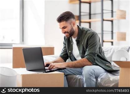 moving, people and real estate concept - happy smiling man with laptop computer at new home. man with laptop computer and moving into new home