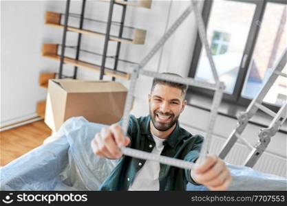moving, people and real estate concept - happy smiling man with ruler in shape of house boxes at new home. happy man with boxes moving to new home