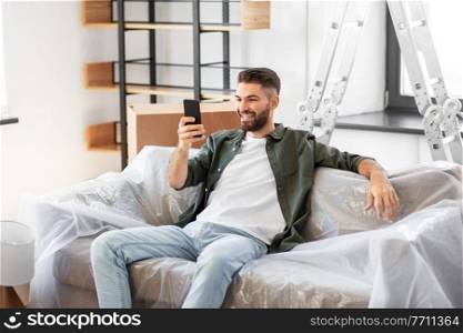 moving, people and real estate concept - happy smiling man with smartphone and boxes at new home. man with smartphone and boxes moving into new home