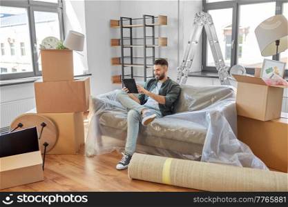 moving, people and real estate concept - happy smiling man with tablet pc computer and boxes at new home. man with tablet pc and boxes moving into new home