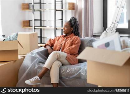 moving, people and real estate concept - happy smiling woman with boxes sitting on sofa at new home. happy woman with boxes moving to new home