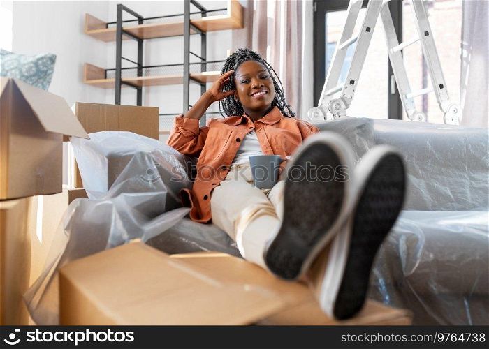 moving, people and real estate concept - happy smiling woman with boxes sitting on sofa with cup of coffee at new home. happy woman with boxes moving to new home