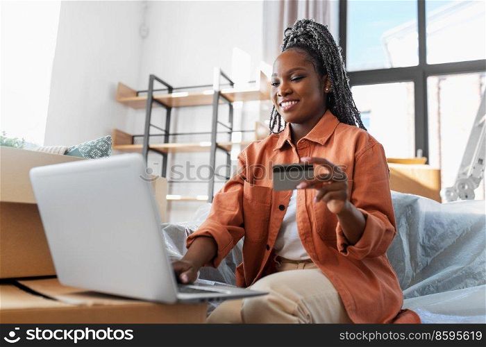 moving, people and real estate concept - happy smiling woman with laptop computer and credit card at new home. woman with laptop and credit card at new home