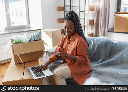 moving, people and real estate concept - happy smiling woman with laptop computer and credit card at new home. woman with laptop and credit card at new home