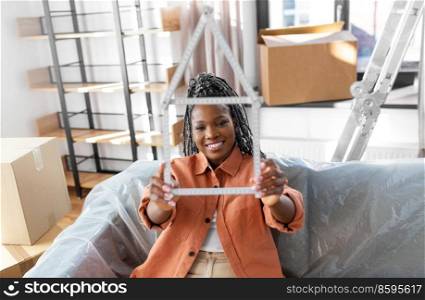 moving, people and real estate concept - happy smiling woman with ruler in shape of house at new home. happy woman with ruler moving to new home