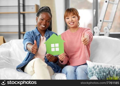 moving, people and real estate concept - happy smiling women holding green house and showing thumbs up at new home. happy women with green house showing thumbs up