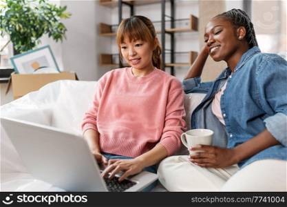 moving, people and real estate concept - happy smiling women using laptop computer and drinking coffee at new home. women using laptop and moving to new home