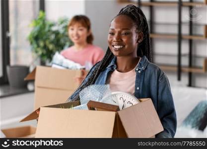 moving, people and real estate concept - happy smiling women with boxes at new home. women with boxes moving to new home
